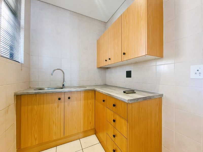 A functional scullery area featuring light wood-finish cabinetry, laminate countertops, a stainless steel sink, and full-height tiled wall finishes.