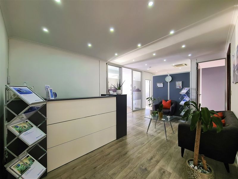 Modern office reception area featuring a built-in reception desk, recessed lighting, laminate flooring, and a glass partition leading to adjacent workspace.