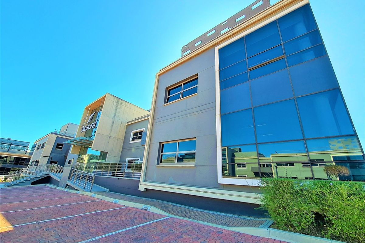 Modern multi-story office building featuring a glass curtain wall facade, concrete architectural elements, and a paved parking area.
