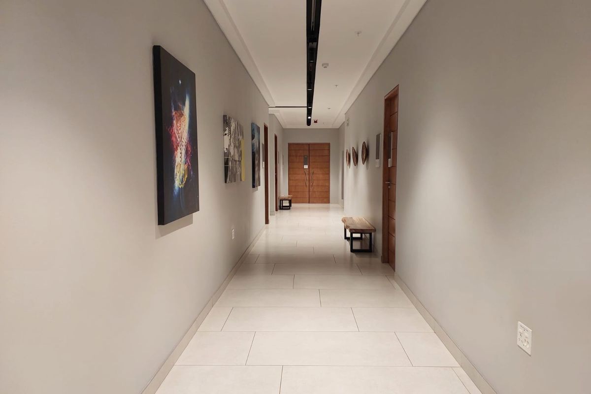 A modern, well-lit commercial hallway featuring neutral tiled flooring, recessed track lighting, and high-quality timber veneer doors.