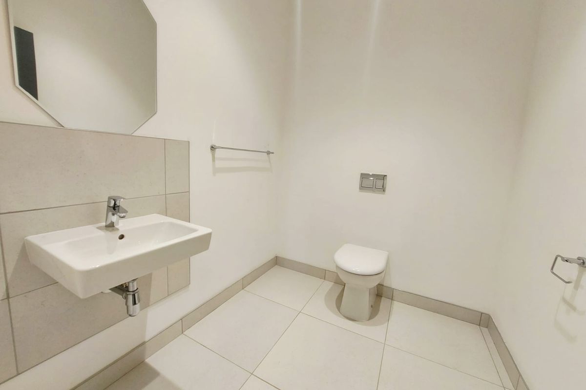 A clean, minimalist commercial bathroom featuring a wall-mounted basin, wall-hung toilet with concealed cistern, and neutral floor tiling.