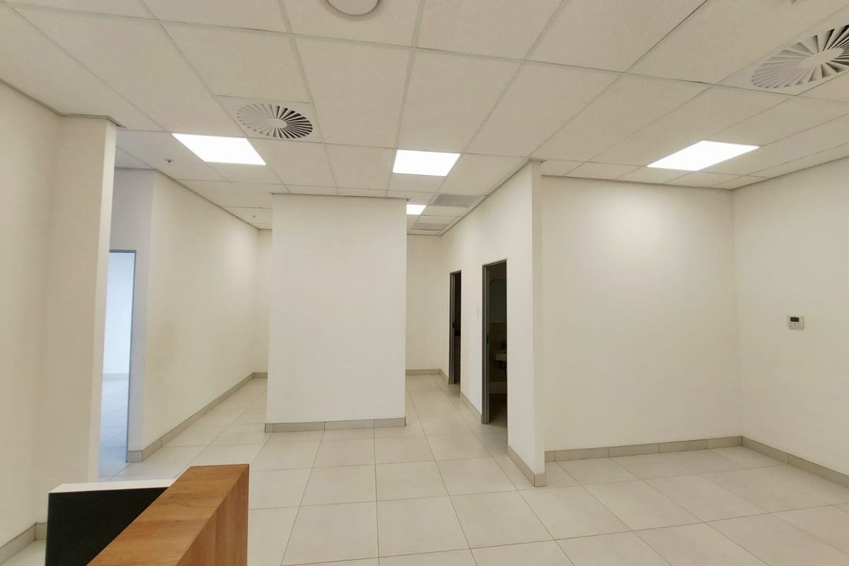 A vacant commercial office space featuring neutral white walls, ceramic tiled flooring, and a suspended ceiling with integrated lighting and air conditioning.