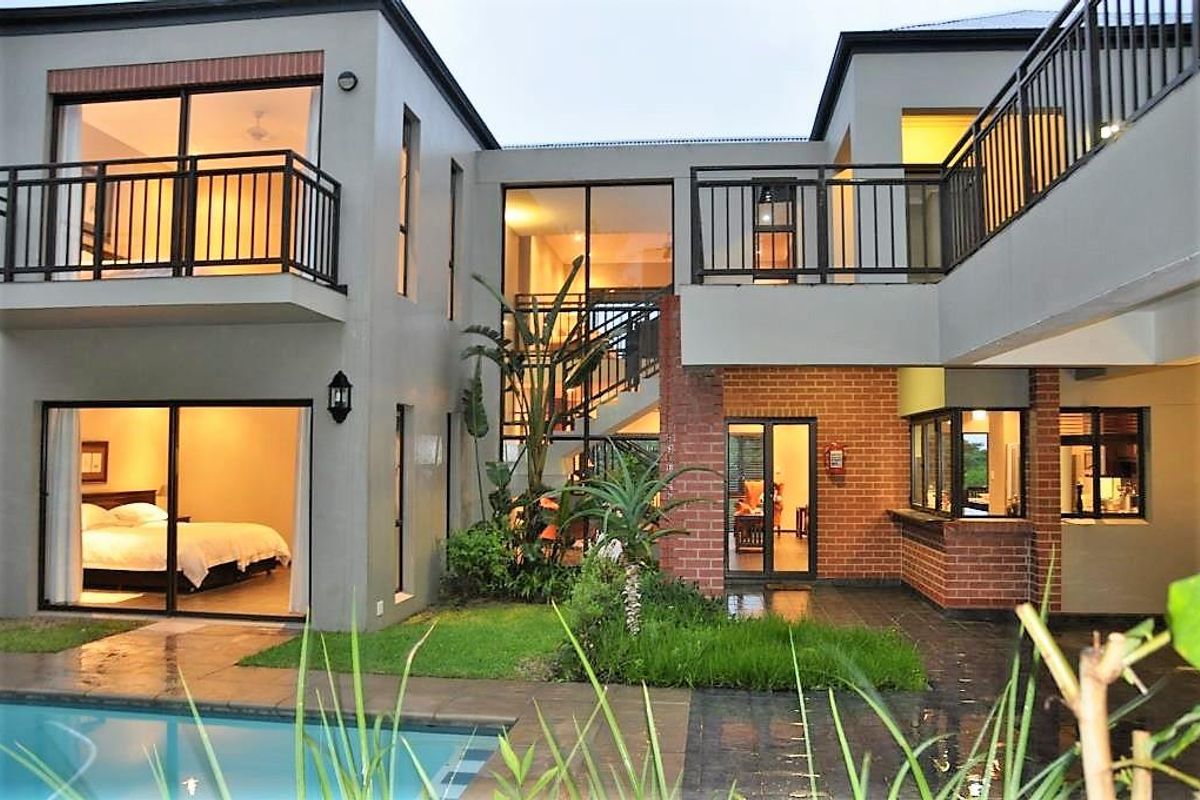 A view of the rear exterior featuring a swimming pool, landscaped garden, balconies, and a multi-level building with brick and rendered facade finishes.
