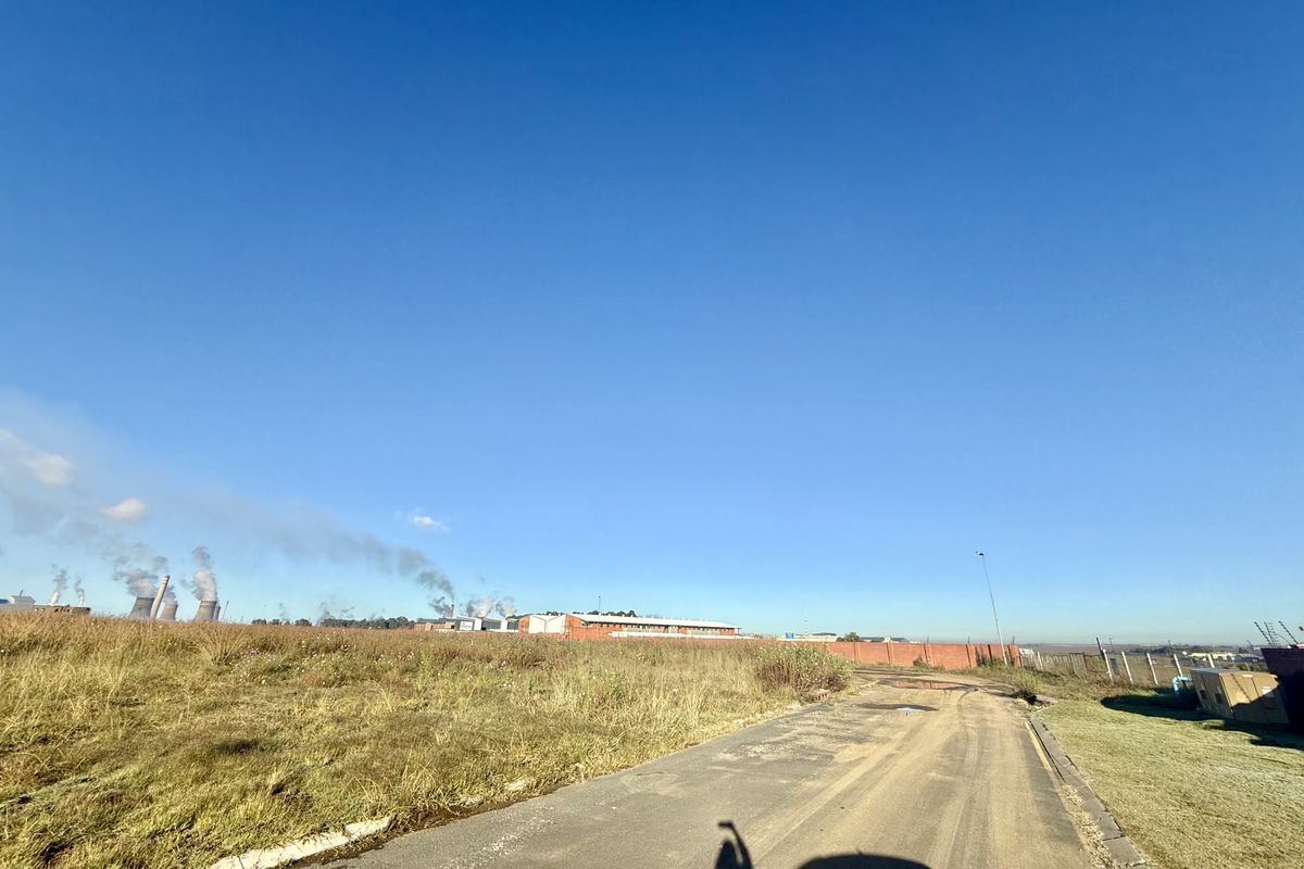A view of the vacant commercial land featuring an access road, perimeter fencing, and surrounding industrial landscape.