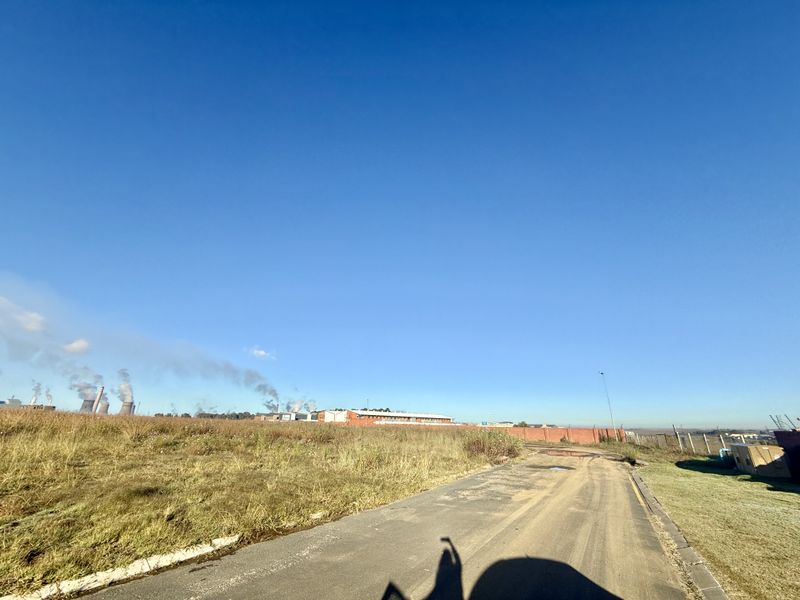 A view of the vacant commercial land featuring an access road, perimeter fencing, and surrounding industrial landscape.