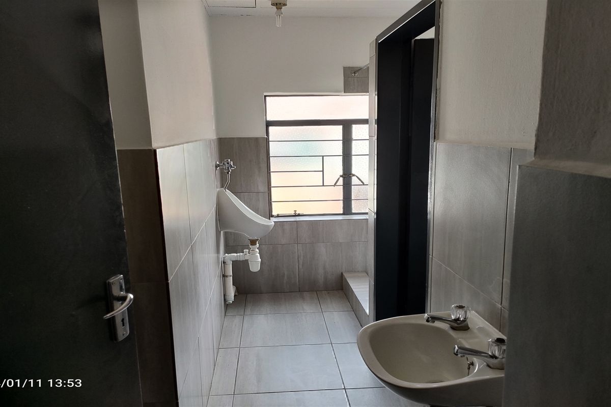 A functional industrial-style restroom featuring tiled walls and flooring, equipped with a wall-mounted urinal and a pedestal basin.