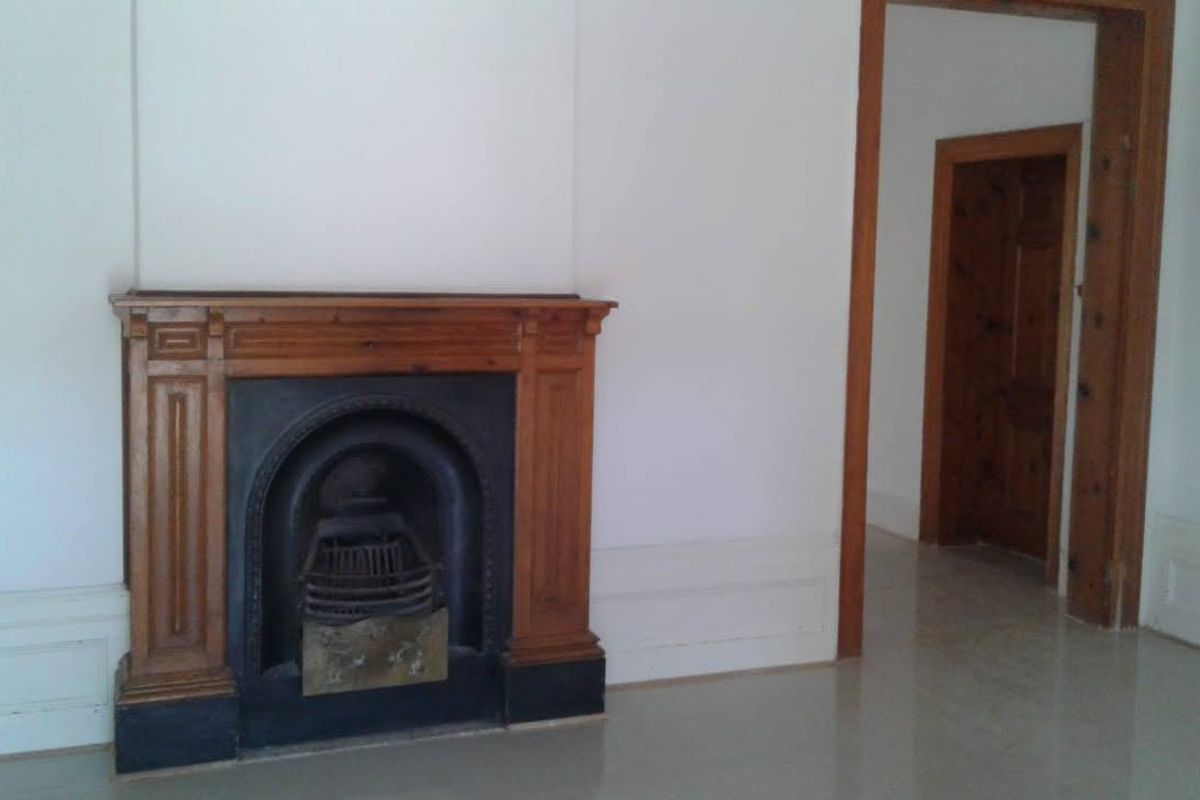 An empty living room featuring a traditional wooden fireplace mantel with a cast iron insert, complemented by wooden door frames and interior doors.
