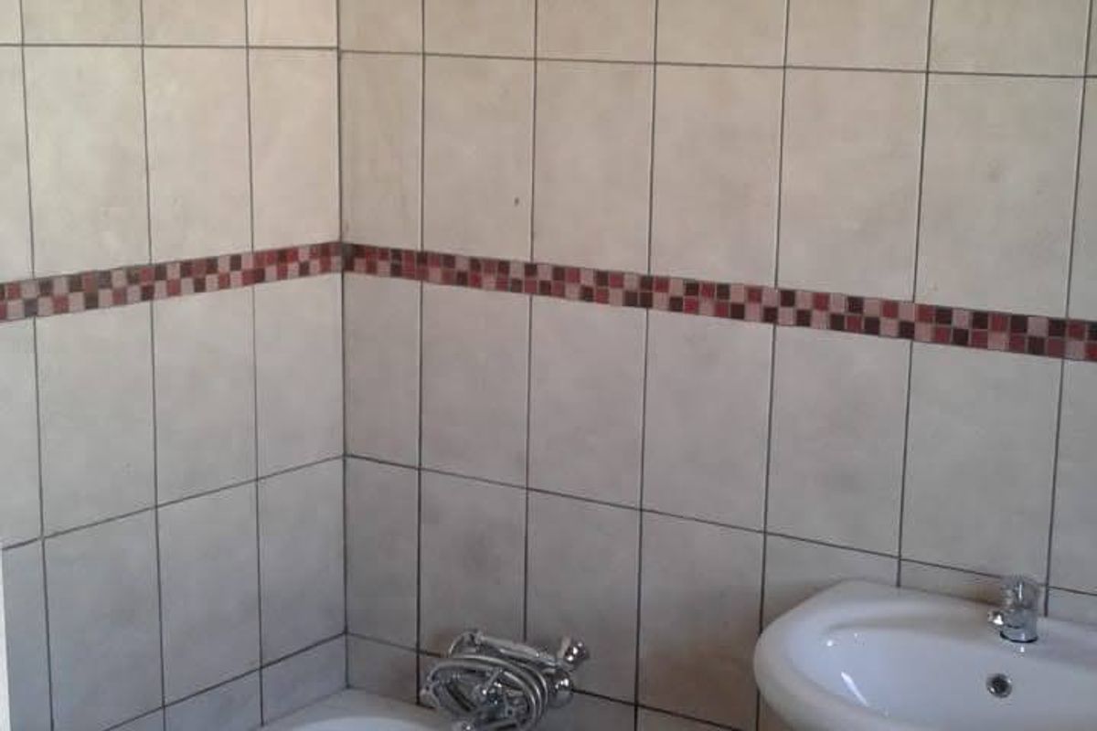 A functional bathroom featuring a pedestal basin, bathtub with chrome fixtures, and neutral ceramic wall tiling with a decorative mosaic border.