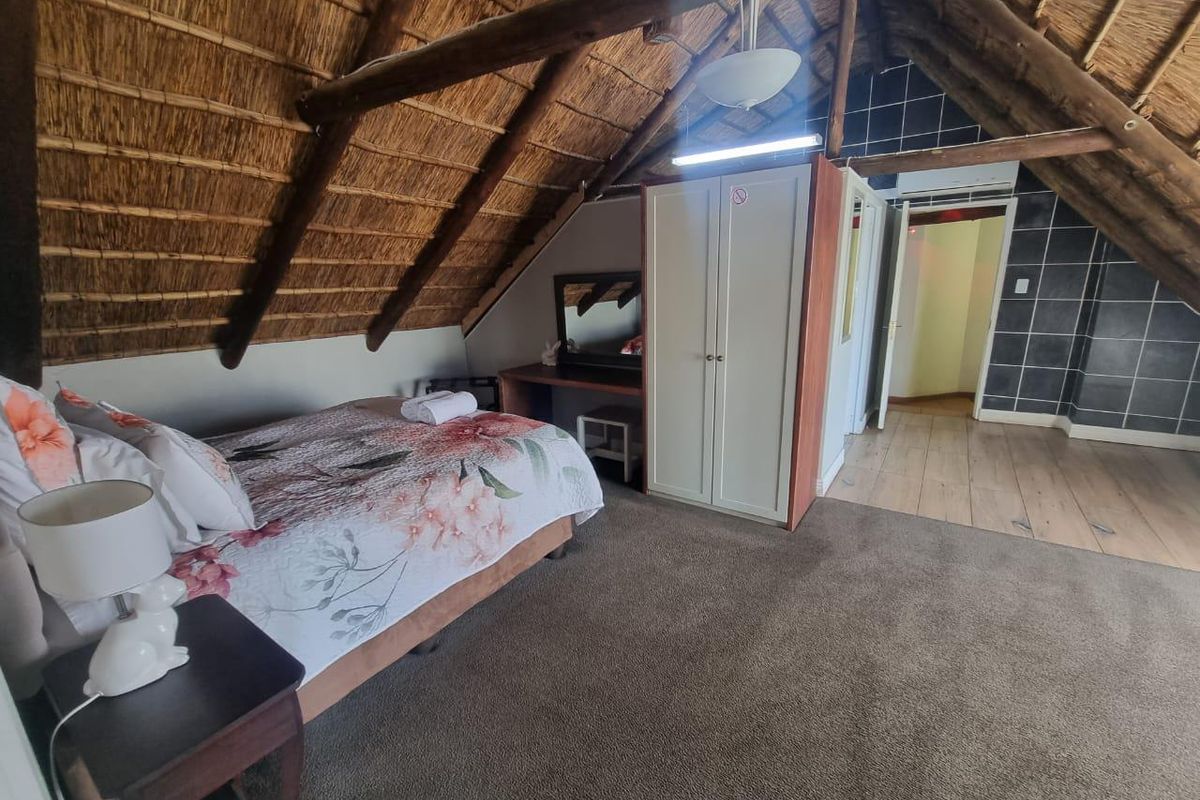 Spacious bedroom featuring a traditional thatched roof with exposed timber beams, carpeted flooring, and built-in cabinetry.