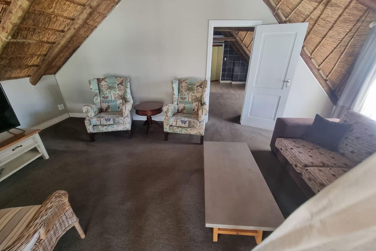 A cozy living area featuring a high-pitched thatched roof, exposed timber rafters, and carpeted flooring, providing a rustic lodge atmosphere.