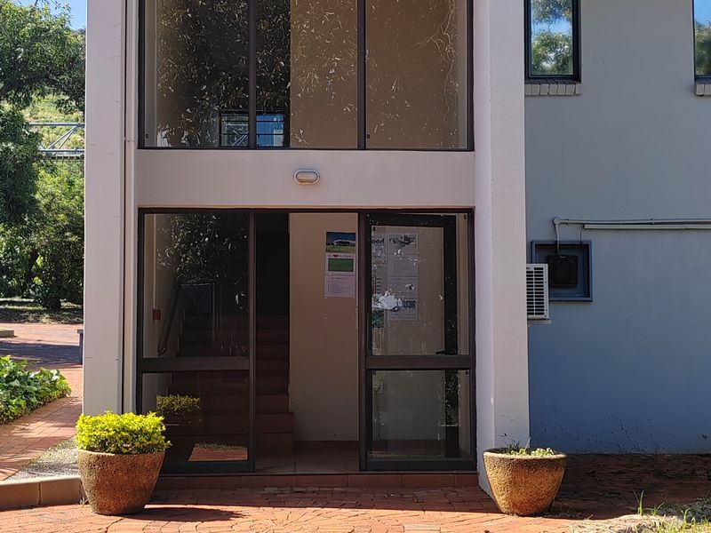 Front entrance of an industrial building featuring a double-height glass facade, brick paving, and metal roof detailing.