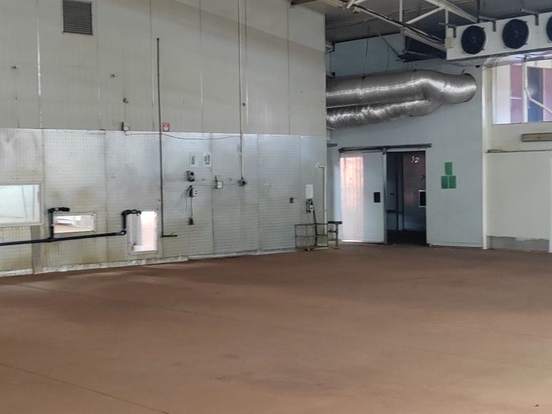 Spacious industrial utility area featuring exposed steel roof trusses, high ceilings, durable concrete flooring, and functional ventilation ducting.