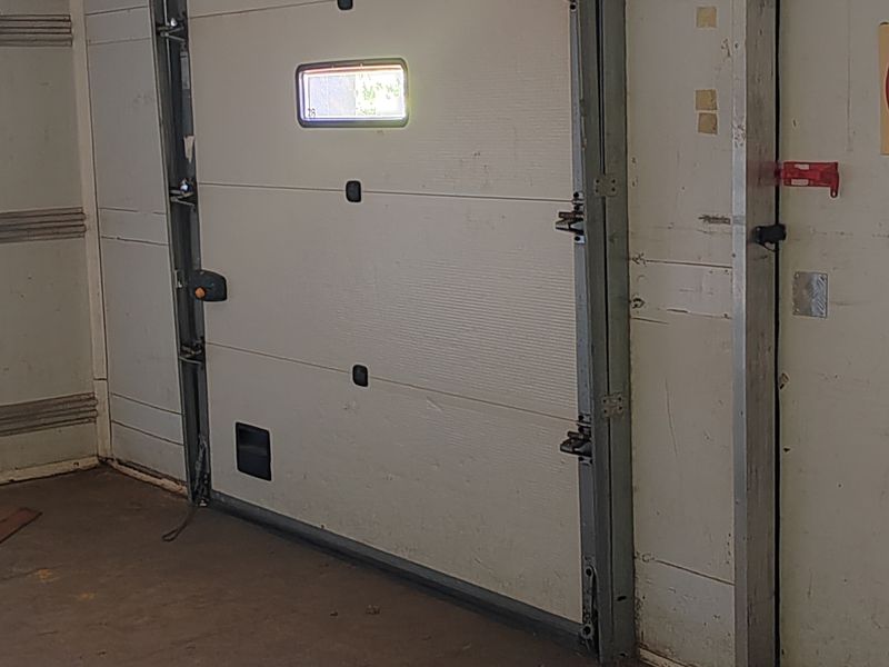 Industrial garage space featuring a sectional overhead door, metal tracking system, and a separate pedestrian access door with concrete flooring.