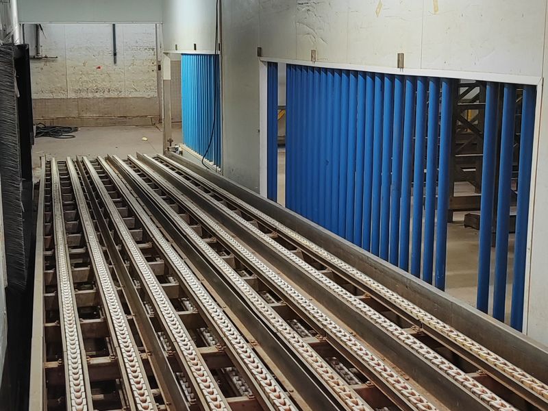 Industrial utility space featuring a built-in conveyor system, insulated wall panels, and overhead fluorescent lighting, suitable for manufacturing or logistics operations.