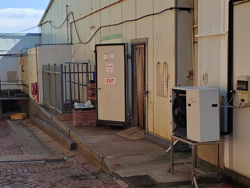Rear industrial exterior view featuring metal cladding, external refrigeration unit, and cobblestone paving with drainage access.