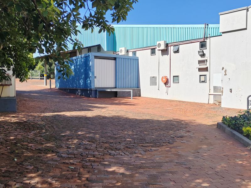 Rear exterior view of an industrial property featuring a brick paved yard, loading bay access, and external wall-mounted air conditioning units.