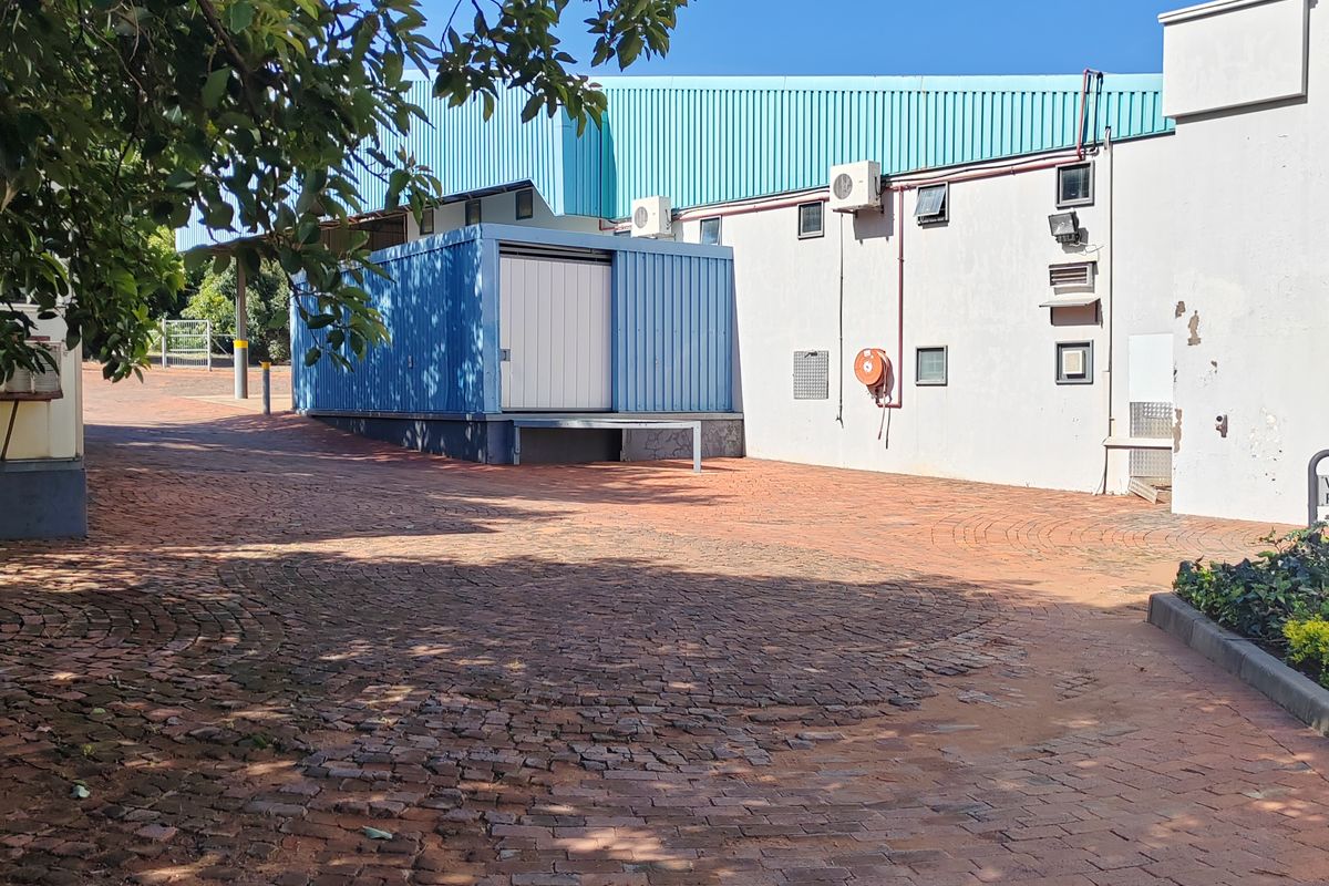 Rear exterior view of an industrial property featuring a brick paved yard, loading bay access, and external wall-mounted air conditioning units.