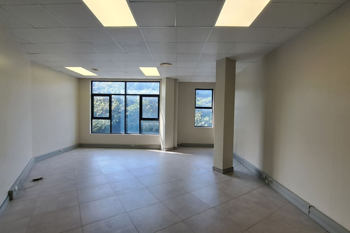 A spacious, empty office suite featuring tiled flooring, a suspended ceiling with recessed lighting, and large windows providing natural light.