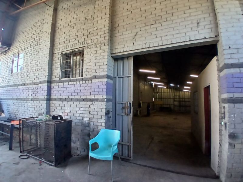 Industrial utility space featuring exposed brick walls, high ceilings with strip lighting, and a large sliding access door.