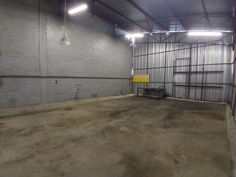 A spacious industrial utility area featuring exposed brick and corrugated metal walls, concrete flooring, and high-clearance steel roof trusses with overhead lighting.