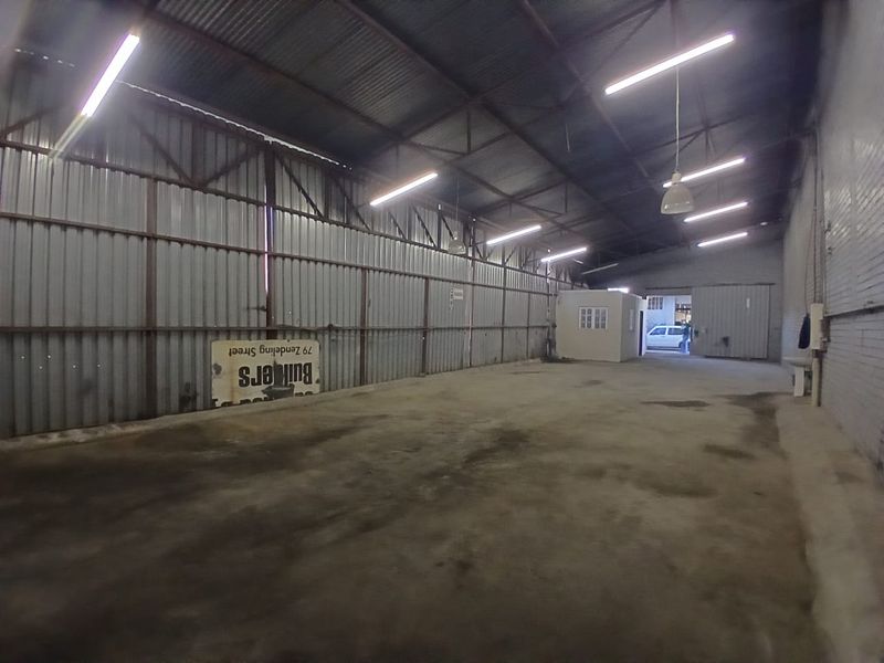 Spacious industrial warehouse unit featuring high ceilings with exposed steel trusses, corrugated metal walls, concrete flooring, and functional strip lighting.