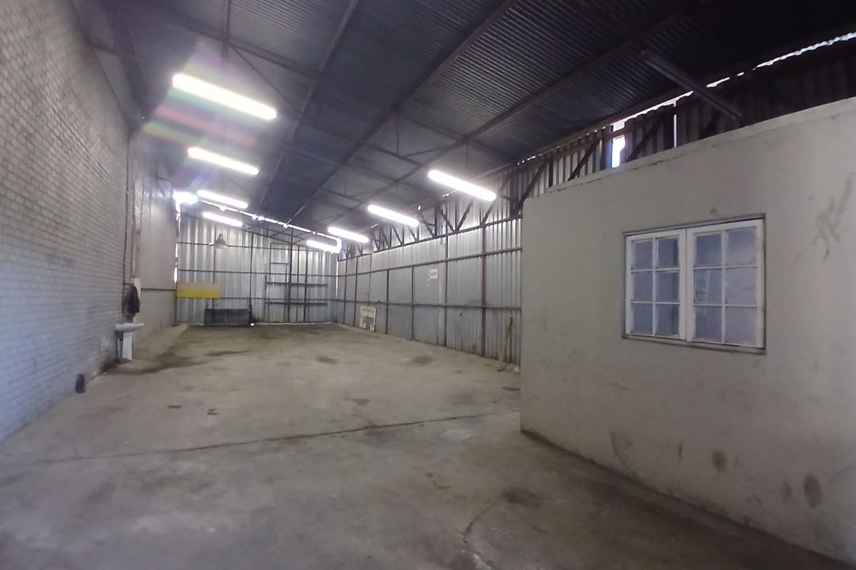Spacious industrial warehouse unit featuring high ceilings with exposed steel trusses, concrete flooring, and an integrated internal office partition.