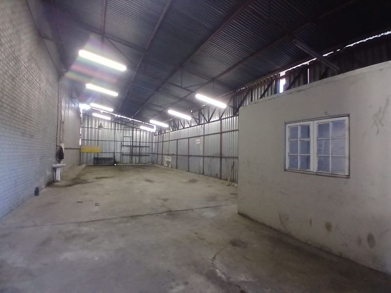 Spacious industrial warehouse unit featuring high ceilings with exposed steel trusses, concrete flooring, and an integrated internal office partition.