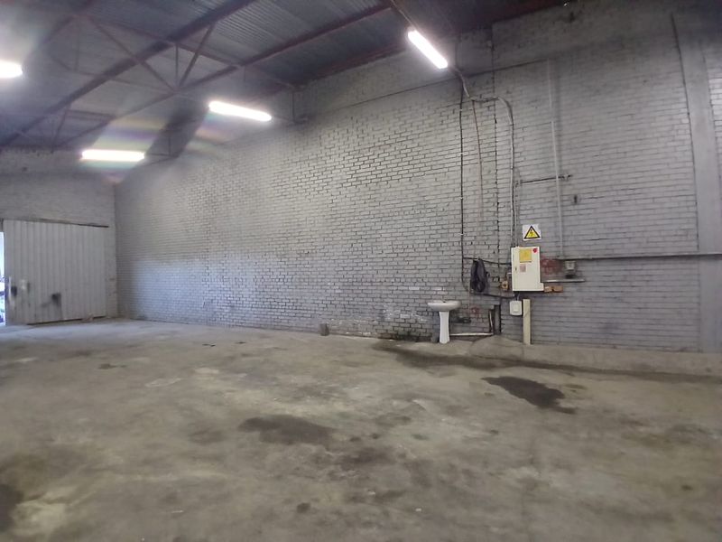 Spacious industrial utility area featuring exposed brick walls, concrete flooring, a pedestal sink, and functional overhead fluorescent lighting.