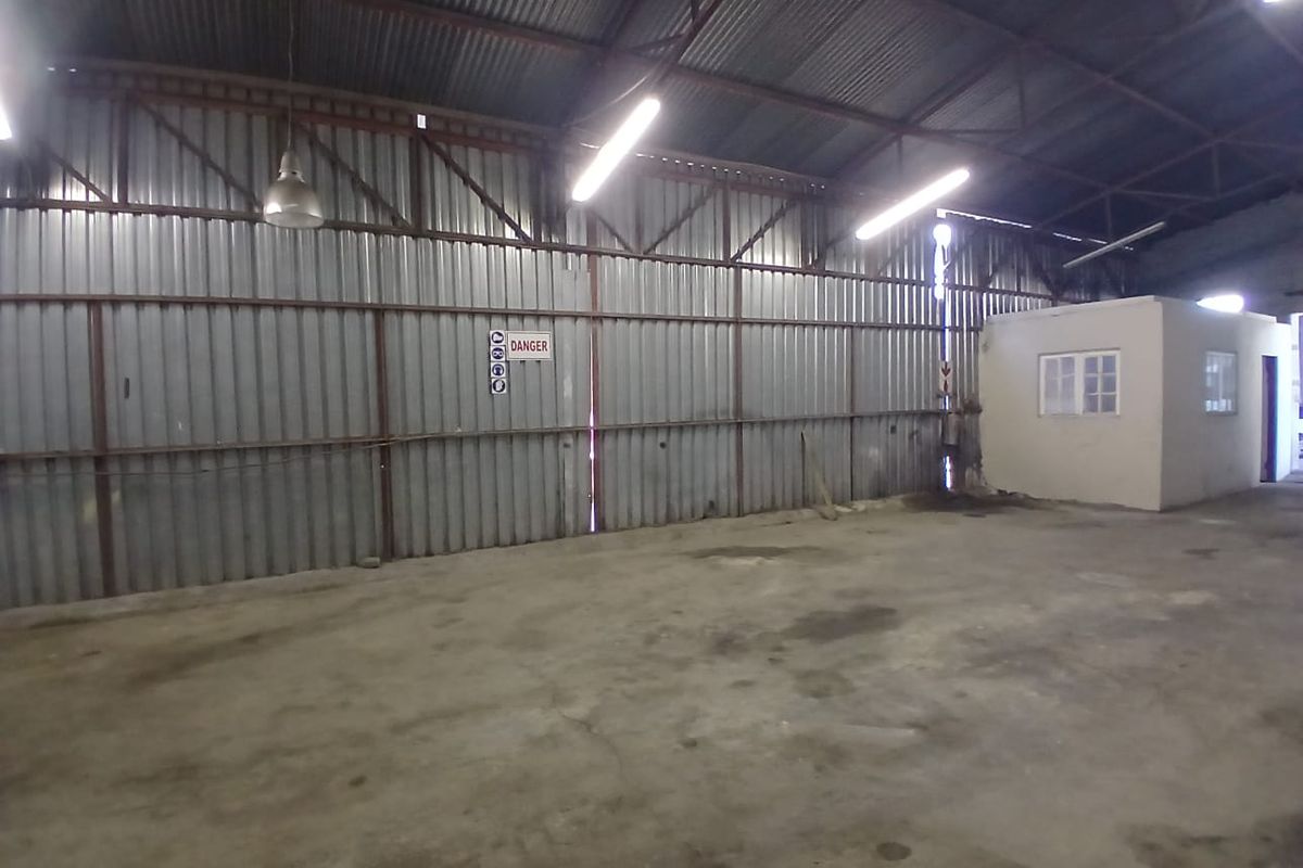 Spacious industrial utility area featuring corrugated metal walls, exposed steel roof trusses, concrete flooring, and an integrated enclosed office structure.