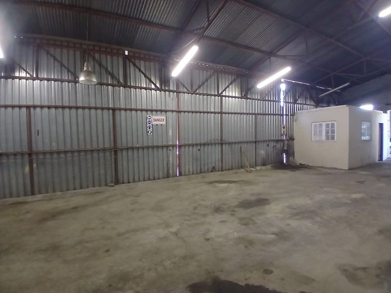Spacious industrial utility area featuring corrugated metal walls, exposed steel roof trusses, concrete flooring, and an integrated enclosed office structure.