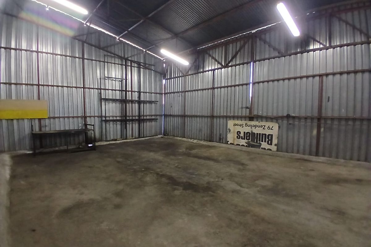 Spacious industrial utility area featuring corrugated metal walls, exposed steel roof trusses, and durable concrete flooring, suitable for workshop or storage use.