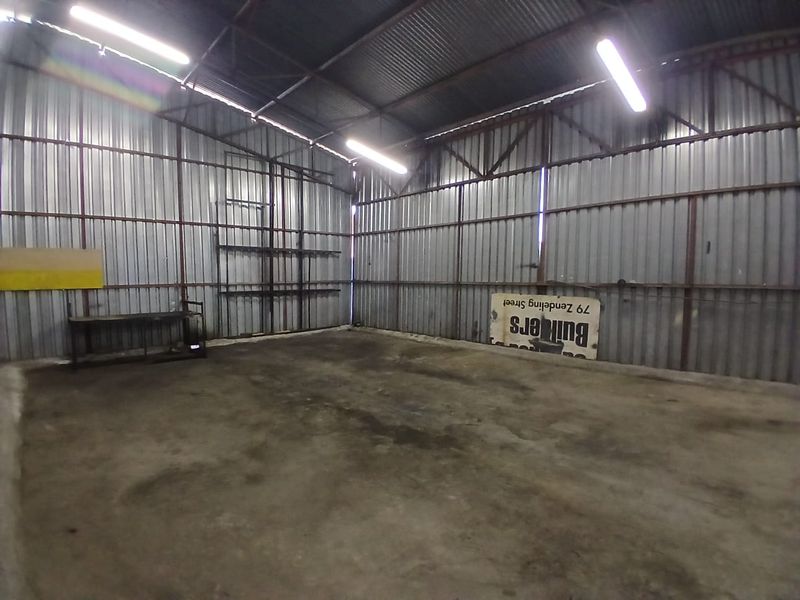Spacious industrial utility area featuring corrugated metal walls, exposed steel roof trusses, and durable concrete flooring, suitable for workshop or storage use.