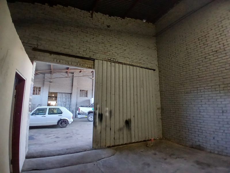 An industrial utility space featuring exposed brick walls, concrete flooring, and a large sliding metal door leading to an adjacent workshop area.