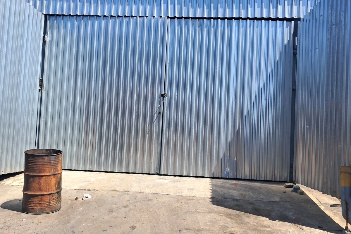 Industrial exterior area featuring large corrugated metal sliding doors and a concrete hardstand, suitable for loading or storage access.