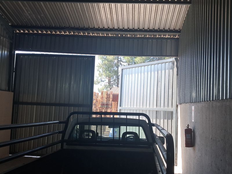 Industrial garage space featuring corrugated metal walls and roof with large swing doors providing access to an outdoor area.