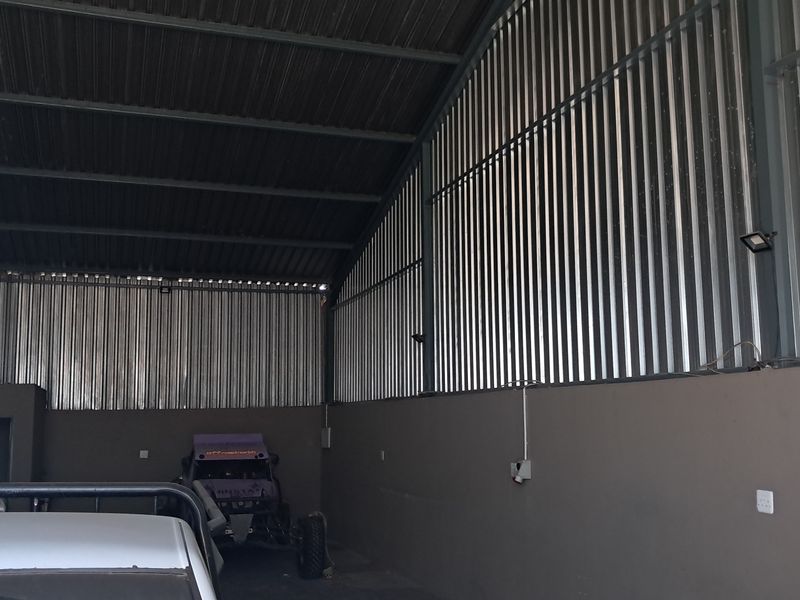 Spacious industrial-style garage featuring high ceilings with exposed steel trusses and corrugated metal wall cladding, providing ample storage or workspace.