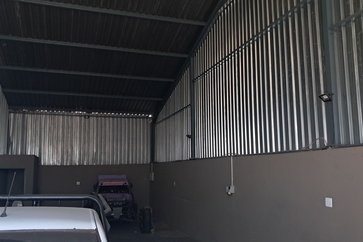 Spacious industrial-style garage featuring high ceilings with exposed steel trusses and corrugated metal wall cladding, providing ample storage or workspace.
