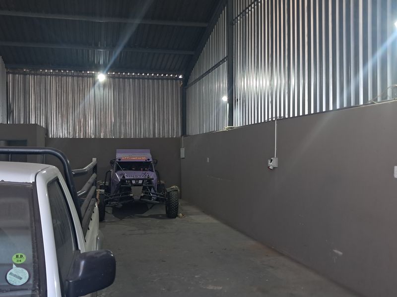 Spacious industrial garage featuring corrugated metal wall cladding, exposed steel roof trusses, concrete flooring, and functional wall-mounted lighting.