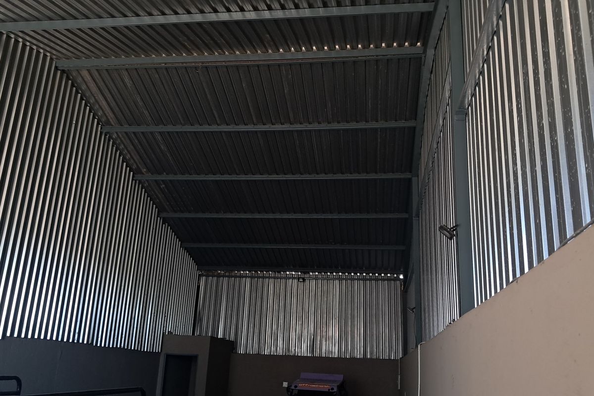 A spacious industrial utility area featuring high ceilings with exposed steel roof trusses and corrugated metal wall cladding.