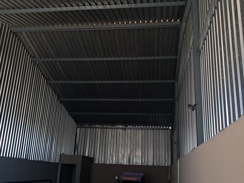 A spacious industrial utility area featuring high ceilings with exposed steel roof trusses and corrugated metal wall cladding.