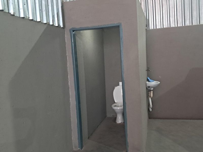 A basic industrial-style bathroom facility featuring a toilet and wall-mounted basin within a partitioned area with corrugated metal wall cladding.