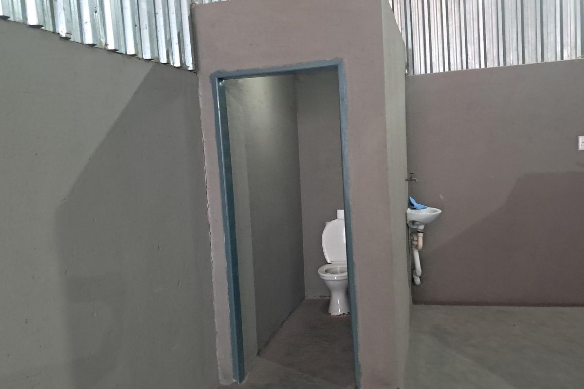 A basic industrial-style bathroom facility featuring a toilet and wall-mounted basin within a partitioned area with corrugated metal wall cladding.