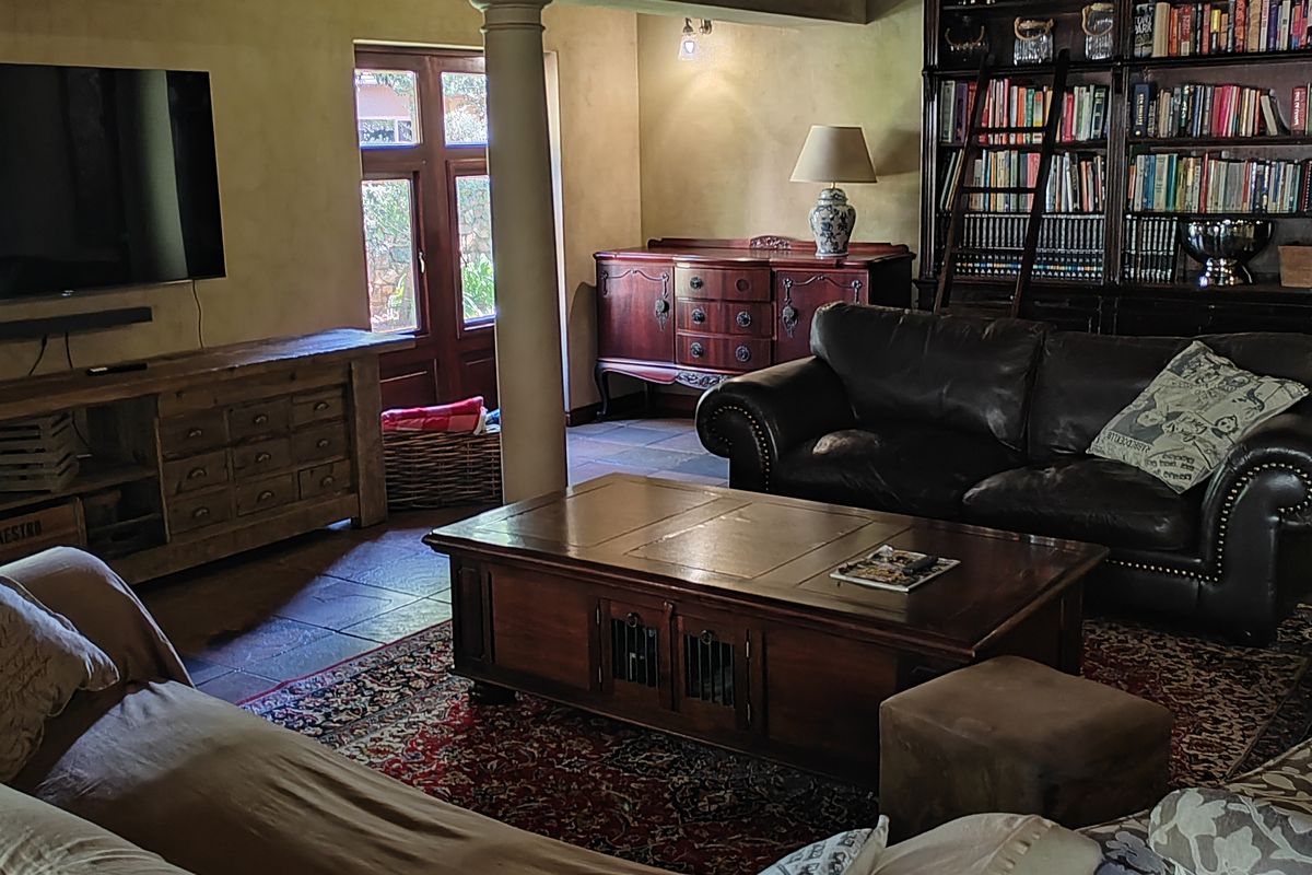 Spacious living room featuring exposed timber ceiling beams, stone tile flooring, and a large built-in floor-to-ceiling bookshelf with a library ladder.