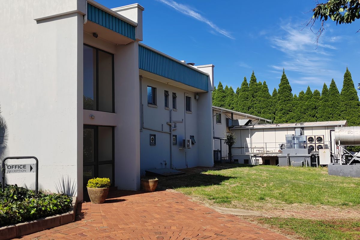 Rear exterior view of the farm property featuring a circular brick paved courtyard, lawn area, and building infrastructure with mounted air conditioning units.