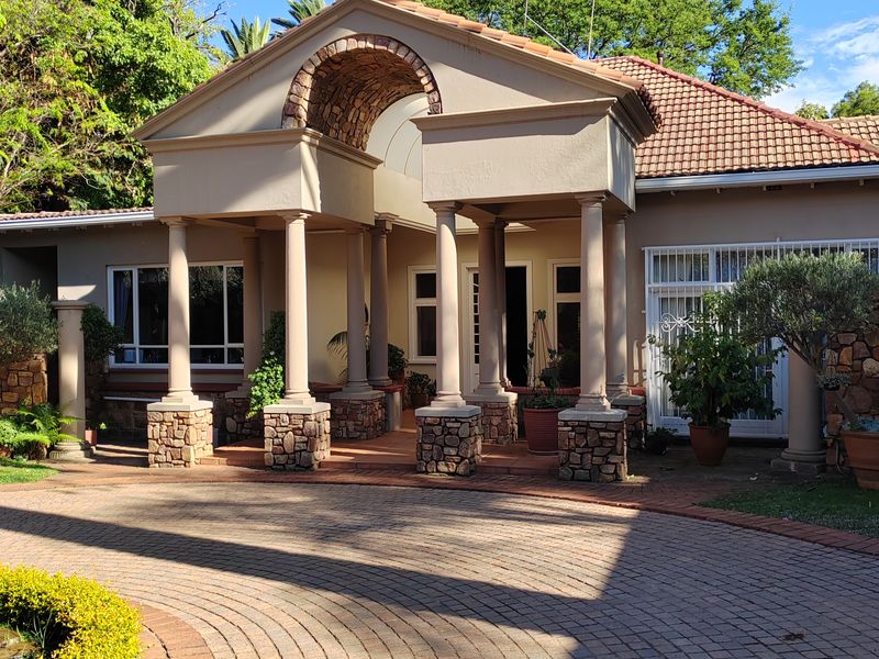 A well-maintained front entrance featuring a grand arched portico with stone-clad pillars and a circular brick-paved driveway.