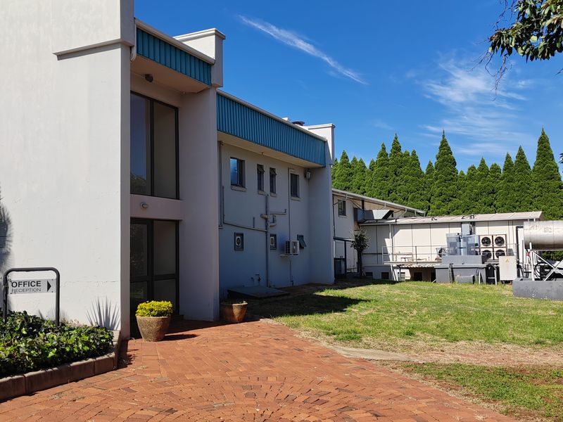 Rear exterior view of the farm property featuring a circular brick paved courtyard, lawn area, and building infrastructure with mounted air conditioning units.