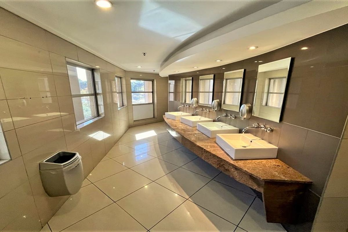 A modern commercial bathroom featuring a long granite vanity with multiple vessel sinks, wall-mounted mirrors, and polished floor tiles.