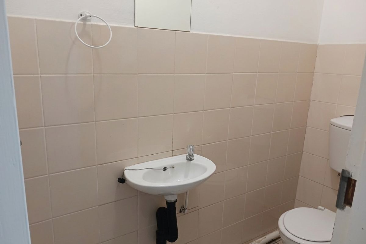 A functional office restroom featuring wall-mounted basin, toilet, and neutral ceramic wall tiling.
