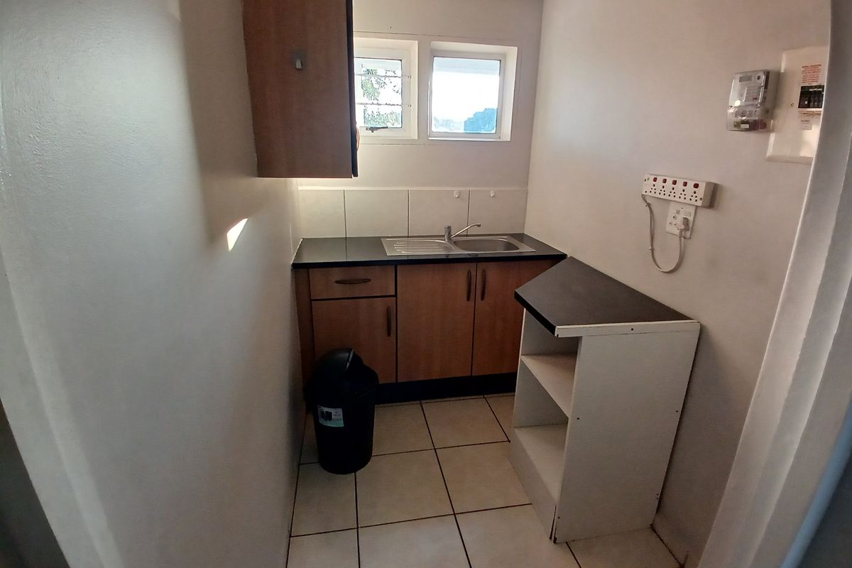 A functional kitchenette area featuring built-in wooden cabinetry, a stainless steel sink, tiled flooring, and a dedicated power point for appliances.