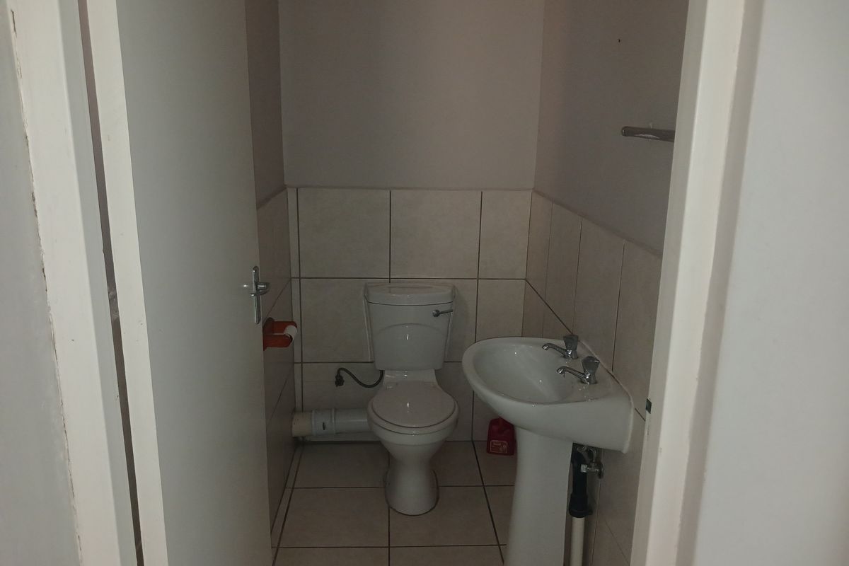 A compact office restroom featuring a standard pedestal basin and toilet with tiled flooring and partial wall tiling.